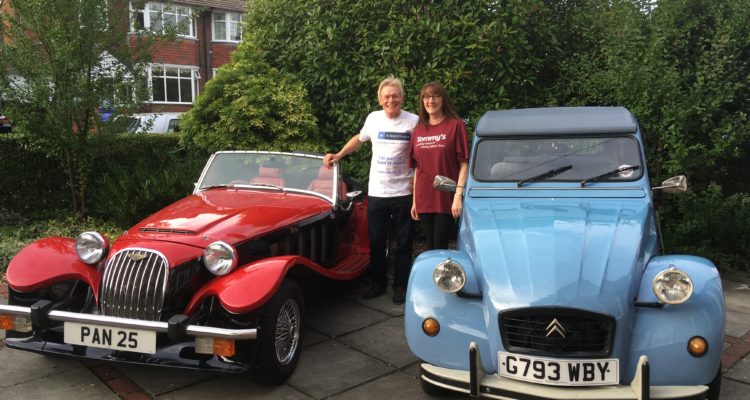 A man and a woman standing next to two classic cars, one is red and one is blue