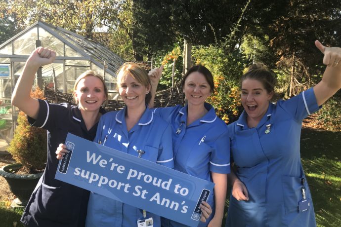 Four nurses holding a sign saying 'We're proud to support St Ann's' and cheering