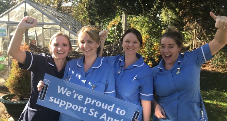 Four nurses holding a sign saying 'We're proud to support St Ann's' and cheering