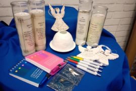 A Light up a Life range of candles, ceramic ornaments, pens and notebooks on a blue cloth.