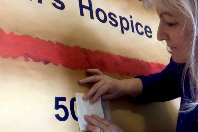 Artist Lindi transferring the number '50' onto a painted wooden cake slice