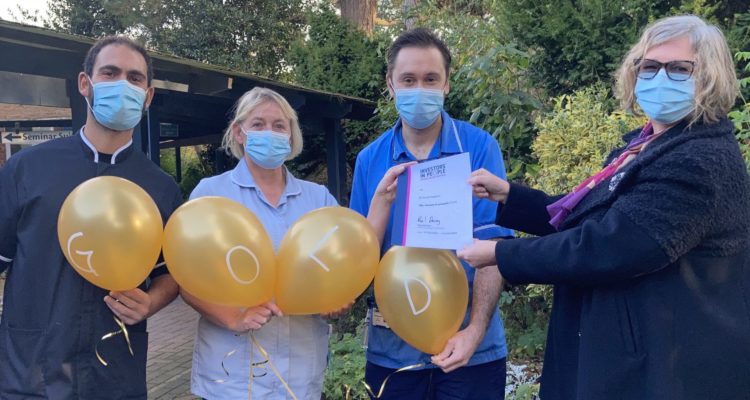 Three staff members and the IIP assessor holding gold balloons which spell GOLD.