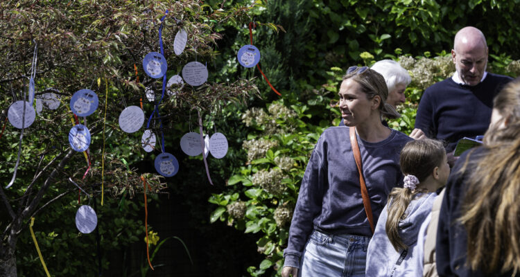 a woman standing next to and looking at a tree, which has paper decorations hanging with ribbons on it
