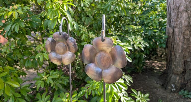 metal flowers hanging on stakes in a flowerbed surrounded by greenery